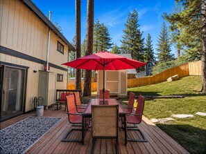 A deck with a table and chairs, a red umbrella, and a wooden fence. - Mama Bear's Cottage - Portable AC, Close to Slopes, Fenced Yard, Pet Friendly (Big Bear Lake)
