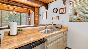 A kitchen with wooden beams, a dishwasher, a sink, and a window with blinds. - Mama Bear's Cottage - Portable AC, Close to Slopes, Fenced Yard, Pet Friendly (Big Bear Lake)