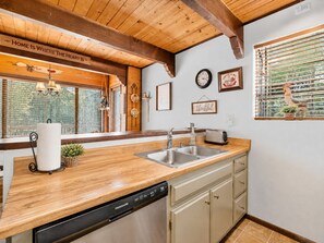 A kitchen with wooden beams, a dishwasher, a sink, and a window with blinds. - Mama Bear's Cottage - Portable AC, Close to Slopes, Fenced Yard, Pet Friendly (Big Bear Lake)