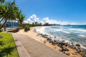 A beach with a paved walkway, palm trees, and ocean waves.