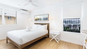 A modern bedroom with a wooden bed, white walls, a ceiling fan, a window with blinds, a bedside table, and a framed picture on the wall.