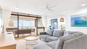 A modern living room with a grey sofa, a round coffee table, and a dining area with a wooden table and chairs.