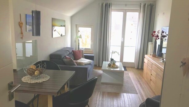 Ein modernes Wohnzimmer mit einer Couch, einem Esstisch mit Stühlen, einem Couchtisch und einer Küchenzeile mit Schränken.