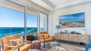 A modern living room with a large window overlooking the ocean, a comfortable seating area, and a flat-screen TV mounted on the wall. - Amazing two bedroom beach front condo W1105 (Puerto Peñasco)