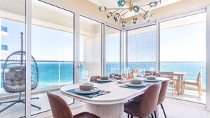 A dining area with a table set for four, overlooking the sea, with a hanging chair and a view of the ocean through large glass doors. - Amazing two bedroom beach front condo W1105 (Puerto Peñasco)