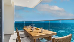 A balcony with a wooden table, chairs, and a glass railing overlooking the ocean. - Amazing two bedroom beach front condo W1105 (Puerto Peñasco)