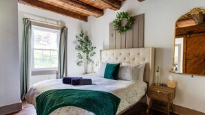 Ein Schlafzimmer mit einem großen Bett, einem hölzernen Kopfteil, einem Spiegel und einem Fenster mit Vorhängen.