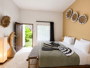 Une chambre d’hôtel comprenant un lit, une table de chevet, une fenêtre avec des rideaux, une porte donnant sur un jardin et des œuvres d’art murales.