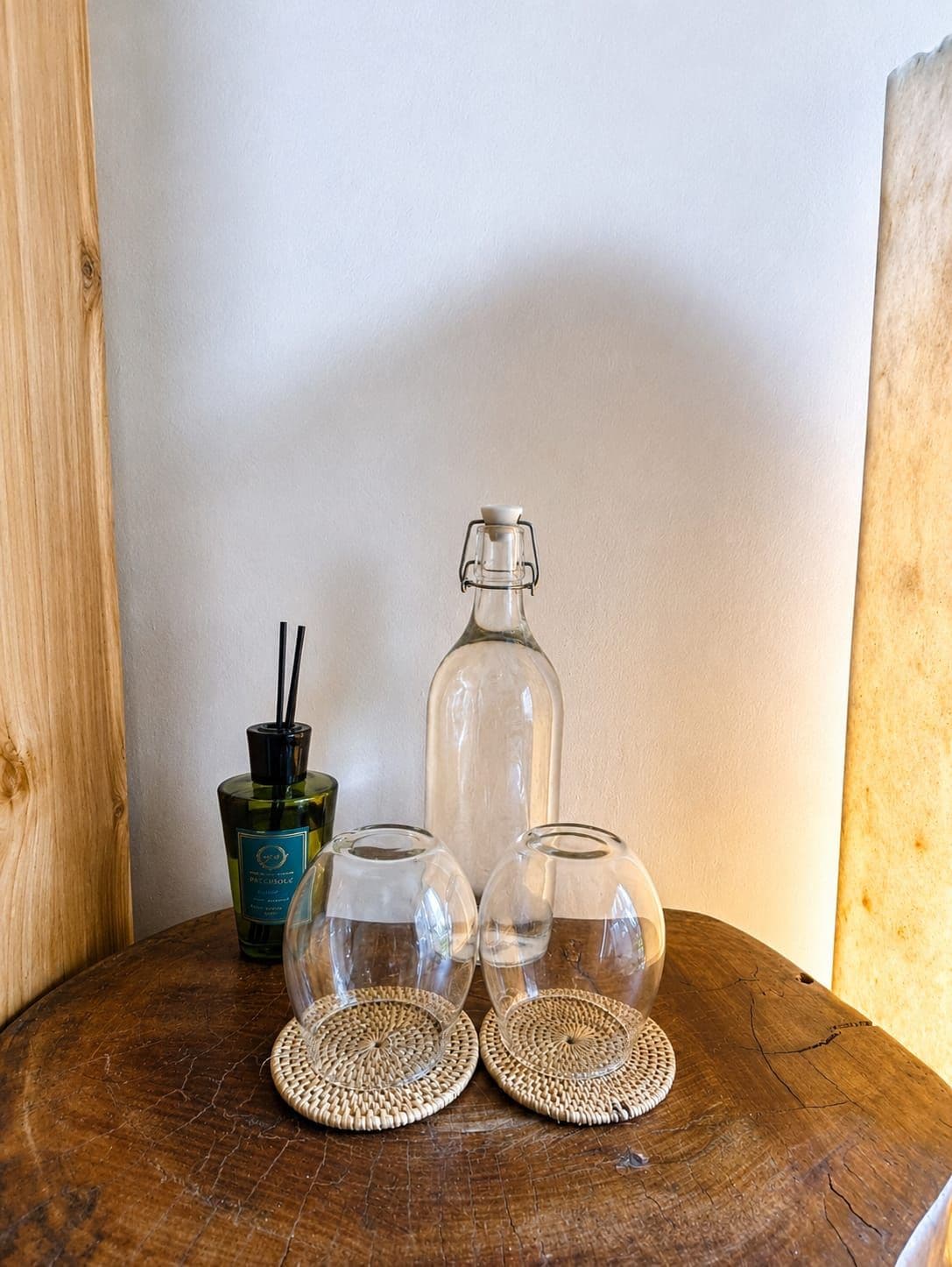 Una mesa de madera con tres vasos de vidrio transparente y una botella con tapón negro.