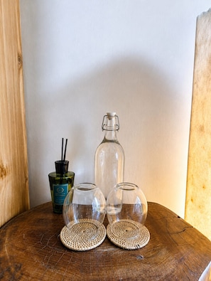 Ein Holztisch mit drei klaren Gläsern und einer Flasche mit schwarzem Verschluss.