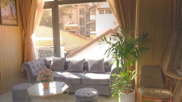 A cozy living room with a grey sofa, a small round table with a vase of flowers, and a potted plant. - Vô Tư Hotel (Xuan Huong - Da Lat)