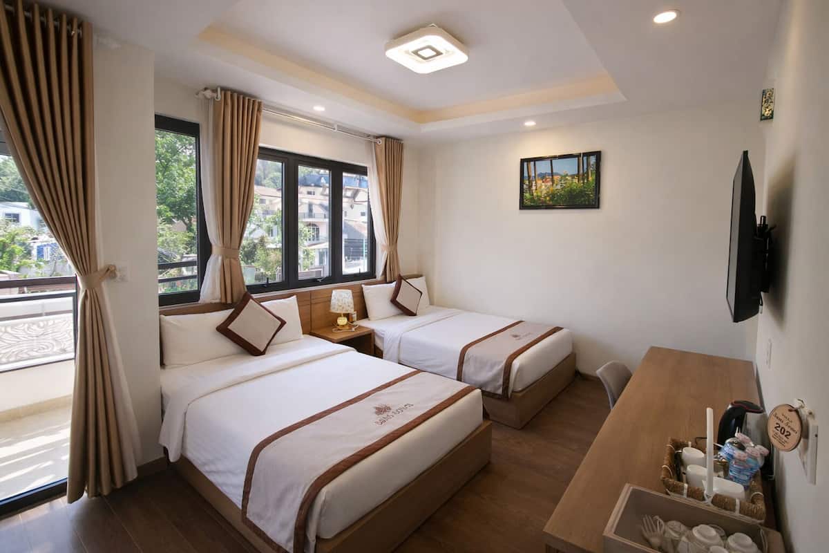 A hotel room with two beds, a desk, a TV, and a window with curtains.