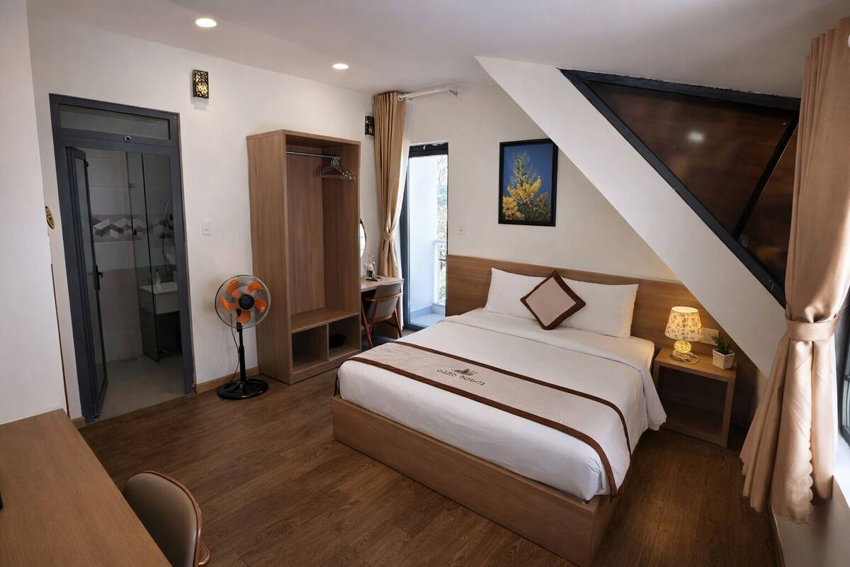 A hotel room with a bed, a desk, a wardrobe, a fan, and a shower.