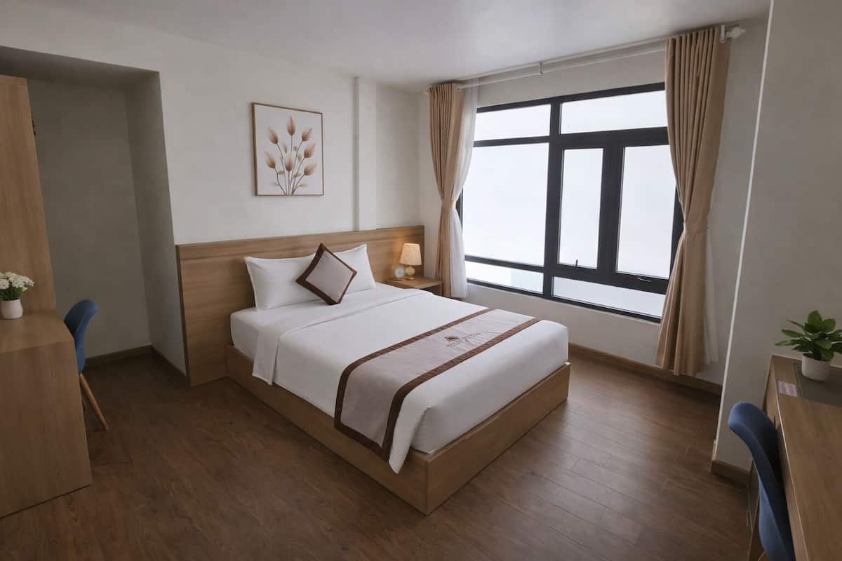 A hotel room with a bed, a desk, a chair, a nightstand, a lamp, a window with curtains, and a wall-mounted picture.