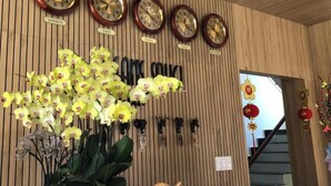 A reception desk with clocks labeled with city names, a potted orchid, and a 'Lê Tân Reception' sign. - Vô Tư Hotel (Xuan Huong - Da Lat)