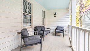 A porch with three gray chairs and a table, white siding, and a lantern.