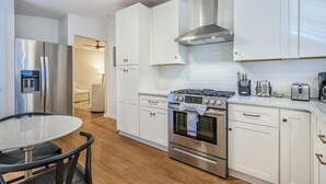 A modern kitchen with white cabinets, stainless steel appliances, and a round dining table.