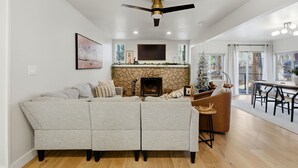 A modern living room with a sectional sofa, a fireplace, a dining area with a table and chairs, and a ceiling fan. - Peaceful Prescott Cabin Near Goldwater Lake (Prescott)