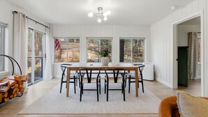 A dining area with a wooden table and chairs, large windows, and a ceiling light fixture. - Peaceful Prescott Cabin Near Goldwater Lake (Prescott)