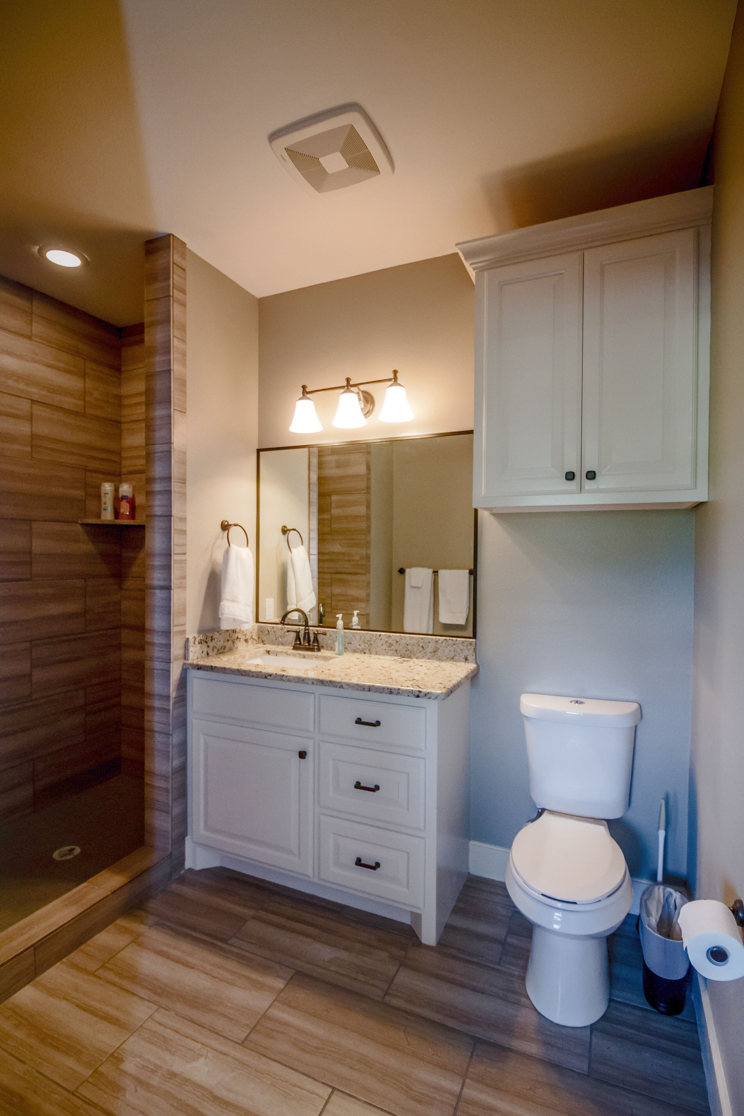 A bathroom with a wooden shower enclosure, a white vanity with a mirror, and a toilet.