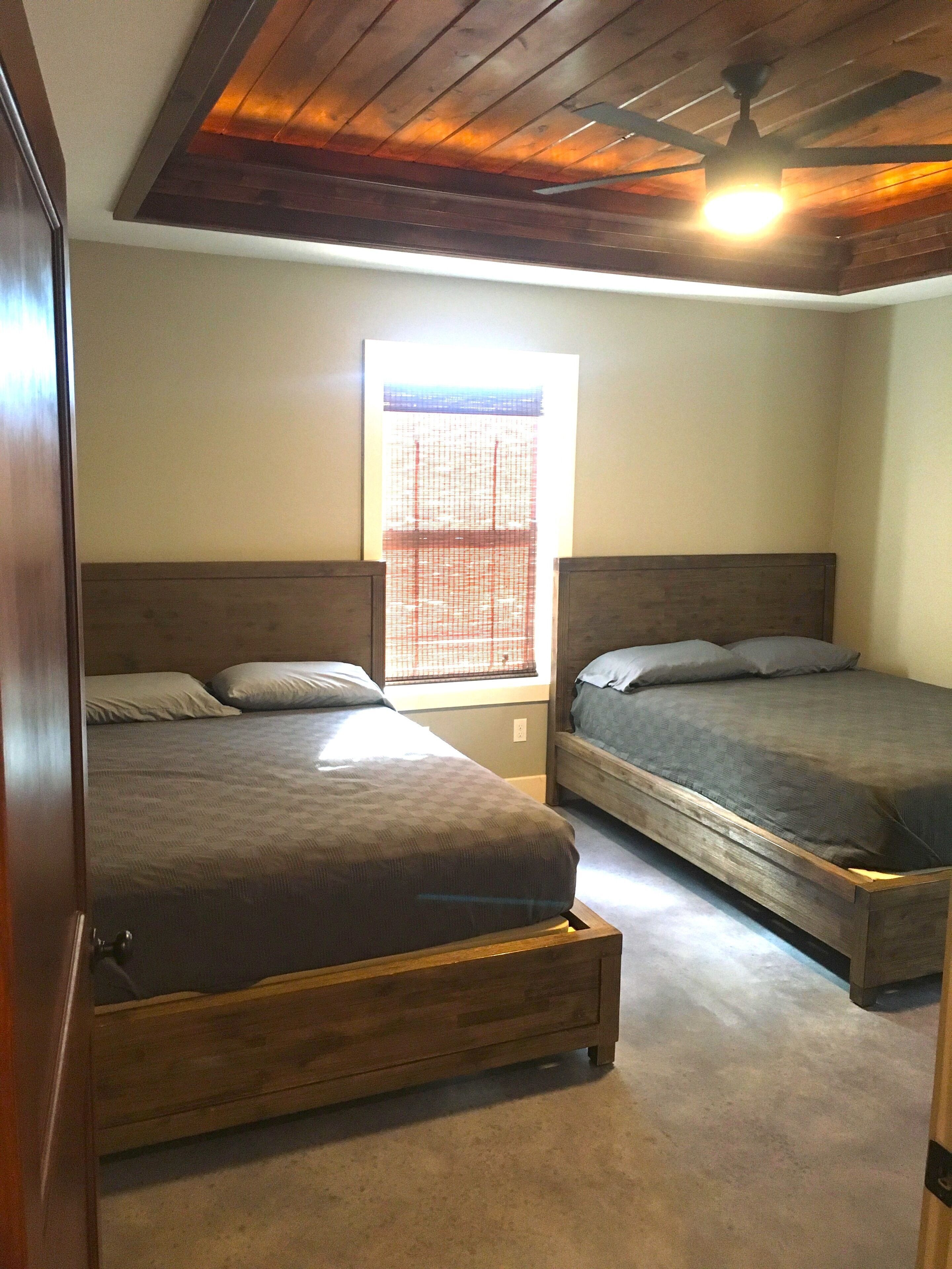 Un dormitorio con dos camas de madera, una ventana con persianas y un ventilador de techo.