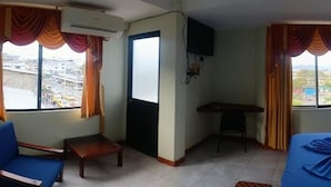 A hotel room with a bed, a desk, a chair, and large windows with curtains. - HOTEL SHEKINAH INTERNACIONAL (Esmeraldas)