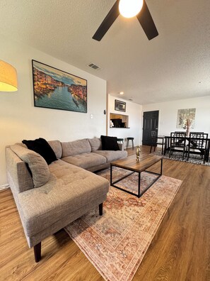 A living room with a sectional sofa, a coffee table, a rug, and a dining area with chairs and a table. - SLEEK LUXE GEM DownTown Dallas 2Bd 2Ba (Dallas)