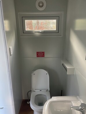 A compact bathroom with a toilet, a window above the toilet, and a sink to the right.