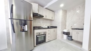A modern kitchen with stainless steel appliances, light wood cabinets, and a tiled floor.