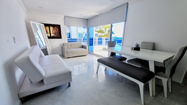 A modern living room with a white sofa, a bench, and a dining table with chairs.