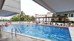 A swimming pool with tiled flooring and a wooden pergola structure.
