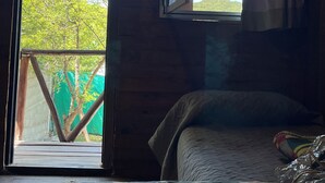 Ein Zimmer in einer Holzhütte mit einem Bett, einem Fenster und Blick auf Bäume.
