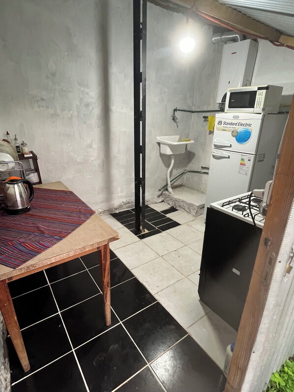 A compact kitchen with a sink, a refrigerator, a gas stove, and a coffee maker on a table.