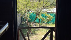 Blick durch ein Fenster mit Metallrahmen auf eine grüne Landschaft mit Bäumen und einem weißen Gebäude.