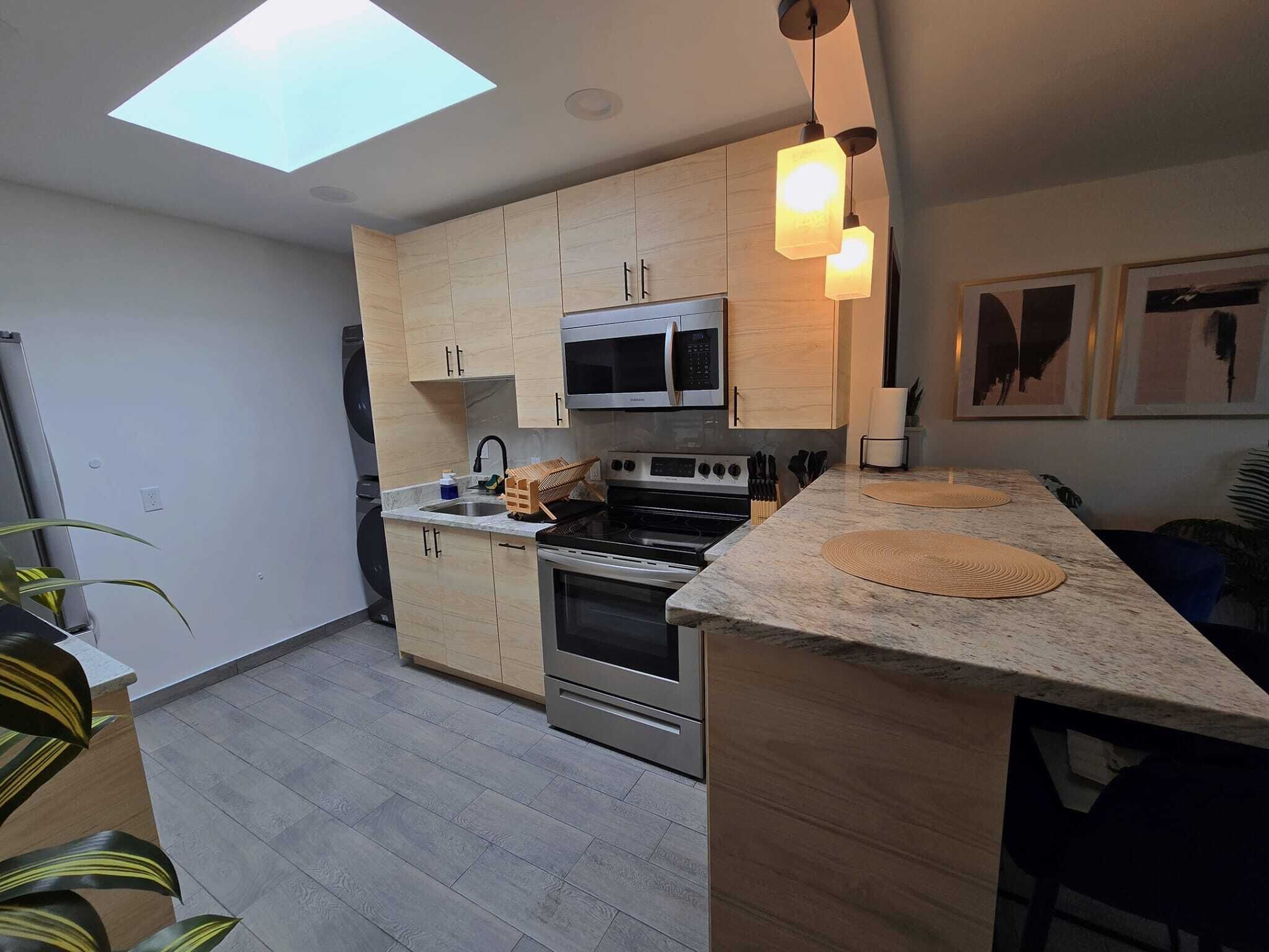 Een moderne keuken met lichte houtkleurige kastjes, roestvrijstalen apparatuur en een dakraam.