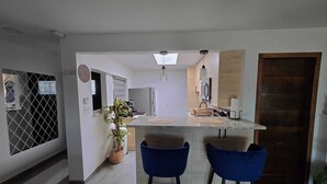 Et moderne køkken med en central ø, to blå barstole og en potteplante.