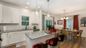 Una cocina moderna con gabinetes blancos, encimeras de granito y una isla central con taburetes de bar.