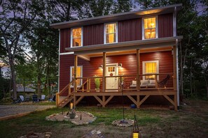 A two-story wooden cabin with a covered porch, a small garden area with rocks and plants, and a visible staircase leading to the upper level. - Whimsical Garden Escape -Fire Pits, Art & Nature Near Asheville (Fairview)