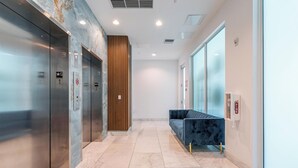 A modern elevator area with two elevators, a wooden panel wall, a blue sofa, and a fire extinguisher. - Charming 2-bedroom apartment with AC, fitness room in Hollywood (Hollywood)