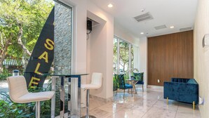 A modern hotel lobby with a glass table, two white chairs, a blue sofa, and a large window with a view of trees. - Charming 2-bedroom apartment with AC, fitness room in Hollywood (Hollywood)