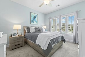 A bedroom with a bed, nightstands, a ceiling fan, a window with blinds, and a painting on the wall. - Coastal Chic  Myrtlewood Condo • Family Comfort & Golf Nearby (Myrtle Beach)