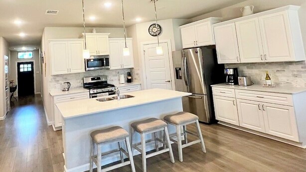 Et moderne køkken med lyse skabe, rustfrie stål hvidevarer og en central ø med barstole.