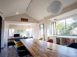 A modern kitchen with a wooden table, yellow and blue chairs, and a large window with a view of trees. - Enjoy with all five senses at this architectdesig / Ito Shizuoka (Ito)