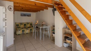 A cozy room with a wooden staircase, a dining area with a table and chairs, a sofa, and a wall-mounted clock. - Apartment Nauzan by Interhome (Saint Palais sur mer)