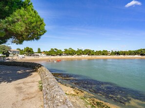 Une scène de plage côtière avec un mur de pierre, une eau claire et une rangée de bâtiments en arrière-plan.