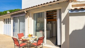 A small outdoor dining area with a table and four chairs, a sliding glass door leading to a kitchen, and a white building with a tiled roof. - Apartment Nauzan by Interhome (Saint Palais sur mer)