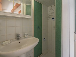 Une salle de bain avec un lavabo blanc, un miroir au-dessus, et un espace douche avec un mur vert.