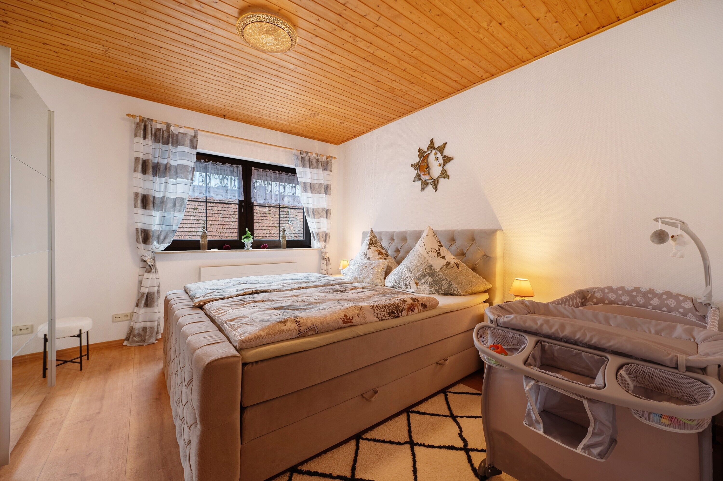 Un dormitorio con una cama, una ventana con cortinas, una lámpara de noche y una cuna.