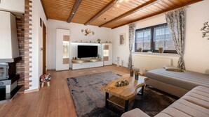 Un salón con chimenea, sofá, televisor y vigas de madera en el techo.