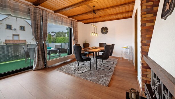 Un comedor con techo de madera, una mesa de comedor con sillas, una alfombra y vistas al exterior.